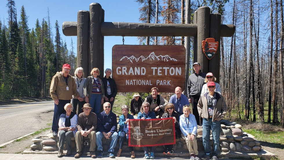 Alumni posing with Brown University banner in front of the Grand Teton National Park sign