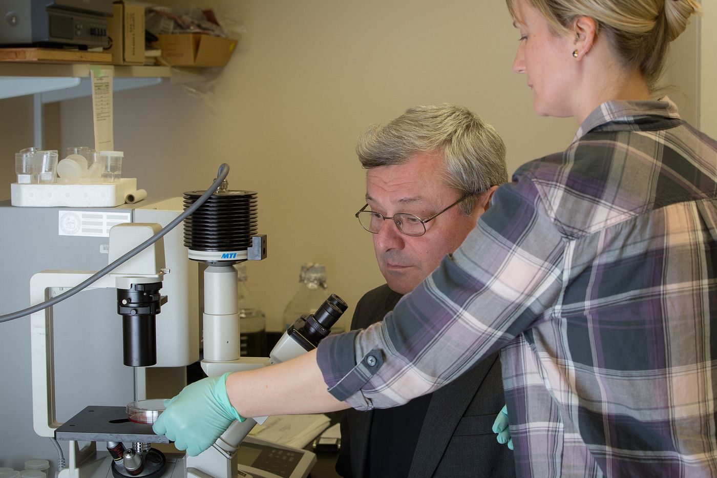 Two researchers are working at a microscope in a lab.