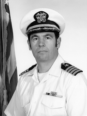 Black and white photo of Richard Edgar '47 wearing his uniform beside an American flag