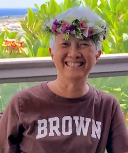 Susan Doyle sitting while wearing a flower crown and a Brown shirt.