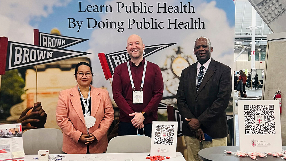 Three people in front of School of Public Health poster