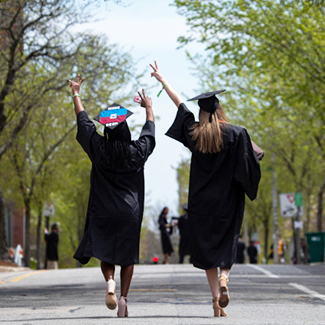 View on campus from behind two new graduates wearing mortarboards and graduation gowns