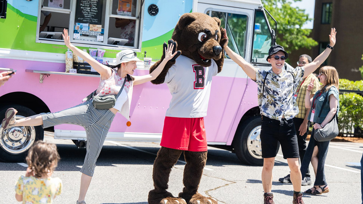 Brown alumni posing with Bruno the mascot in front of a food truck at Bruno's Block Party