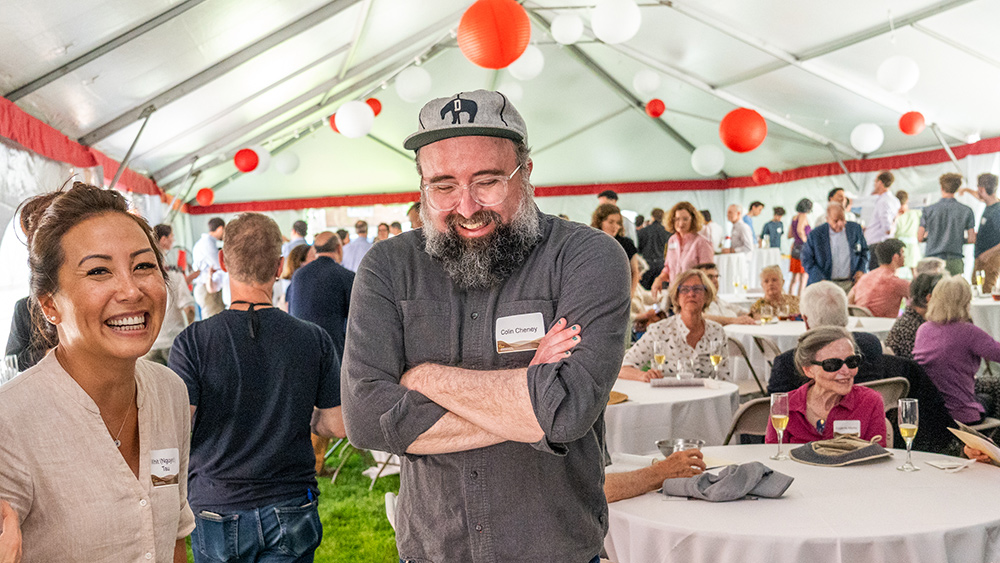 Two alumni smiling at a reception under a tent with white and red lanterns hanging above