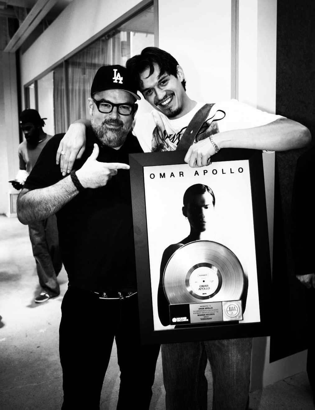 Nate Albert standing alongside singer Omar Apollo as he holds up a music record plague