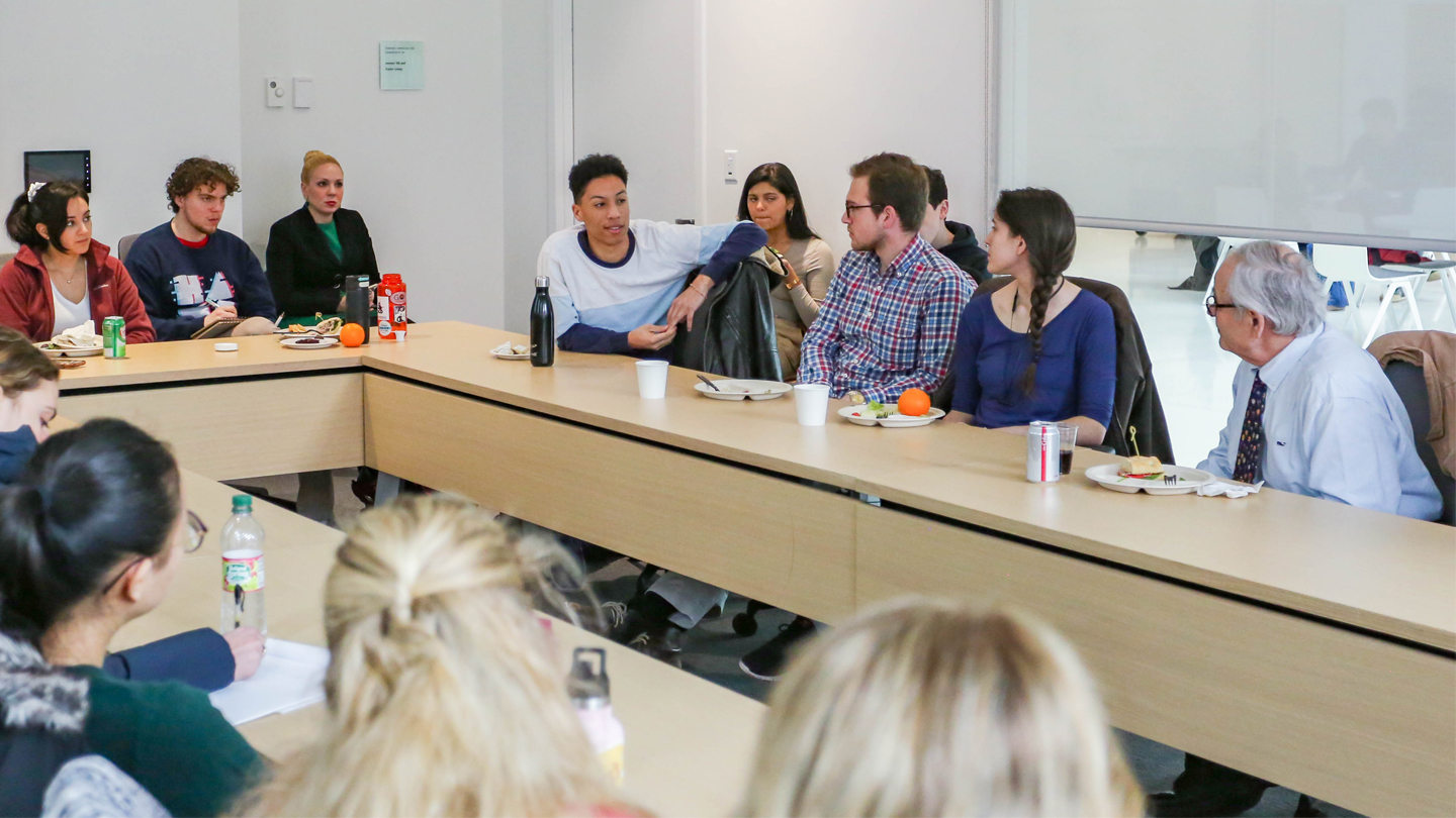 Students around a horseshoe shaped table during a class discussion.