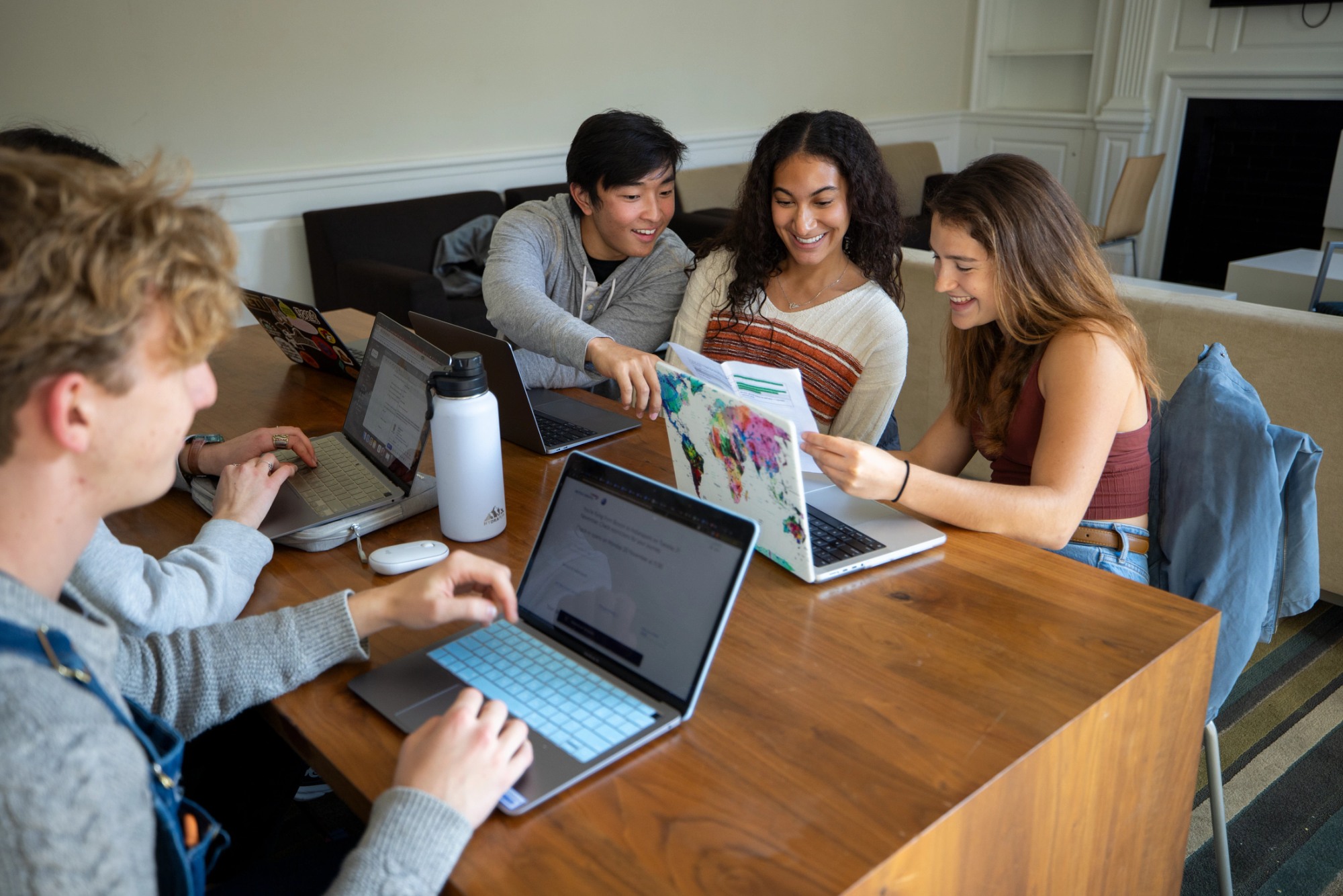 Four studnets sitting at a wooden table on their laptops.