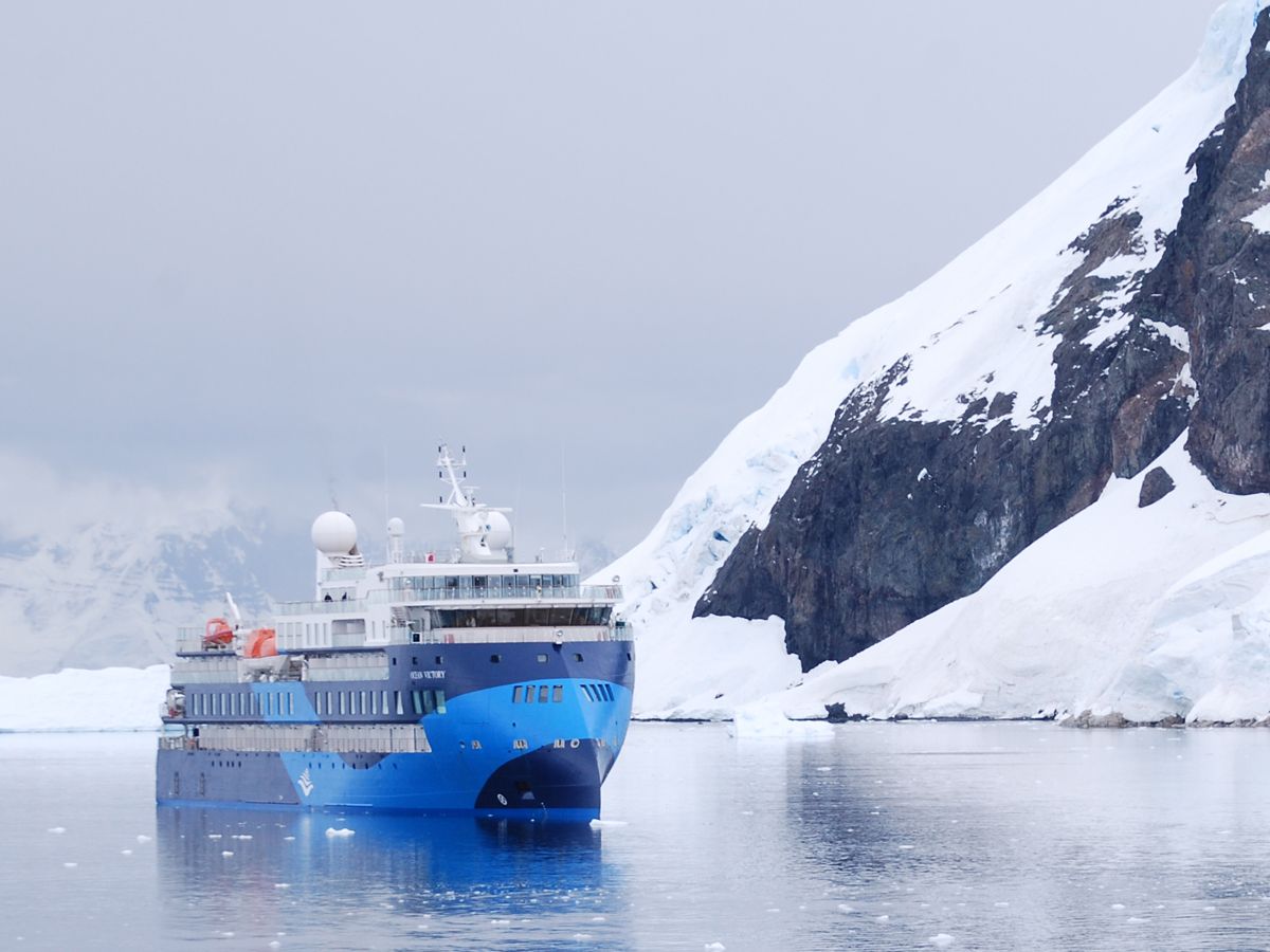 A cruise ship sails across placid waters along the Antarctic coast.