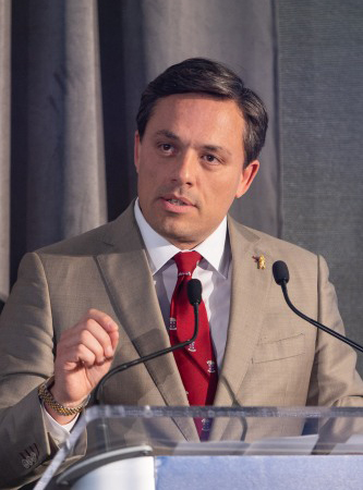 A photo of Carlos Lejnieks behind a podium.