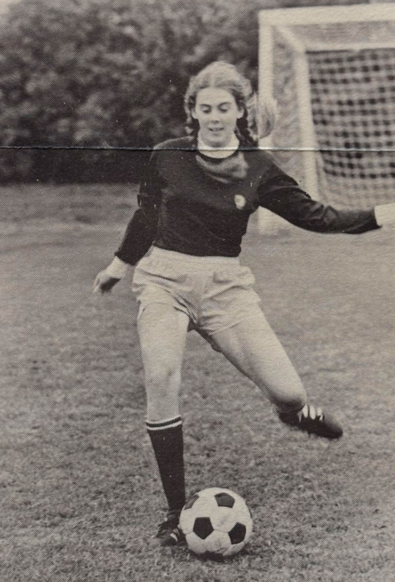 A black and white photo of Amanda kicking a soccer ball on a field. 