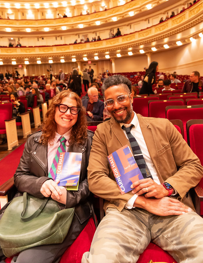 Two people seated in an concert hall holding programs that say "Carnegie Hall." 