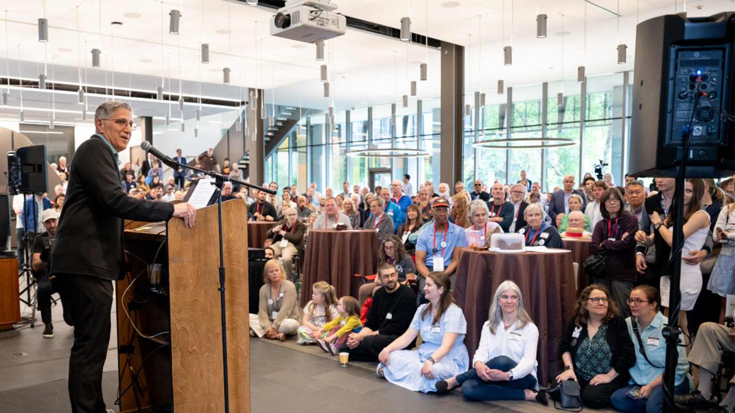 Thanos Chaltas speaking at the podium in front of the crowd of attendees.