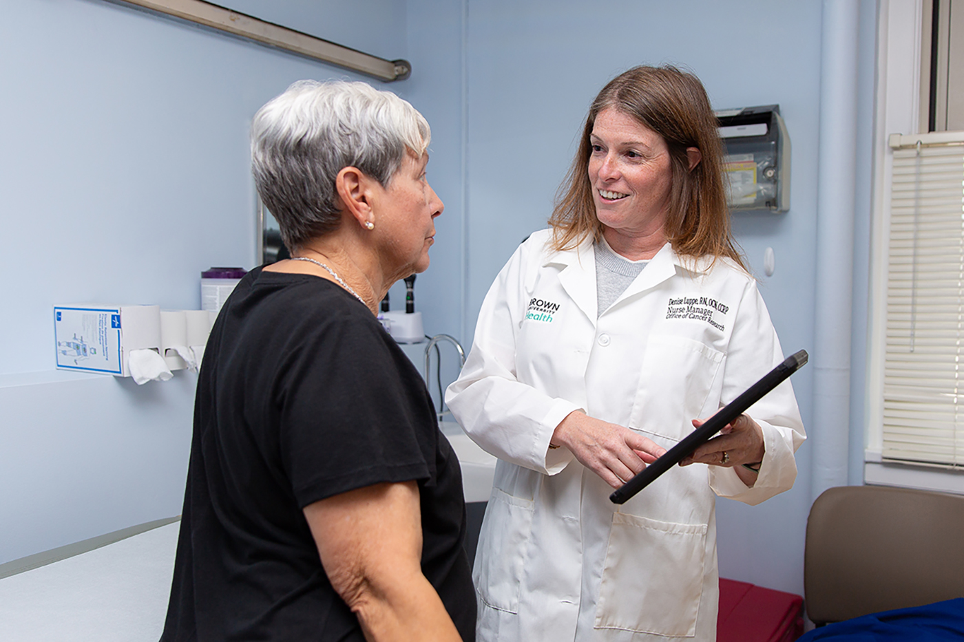A provider is speaking to an elderly patient and pointing to an iPad.