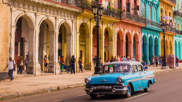 Taxi driving through Habana Vieja in front of a colorful facade