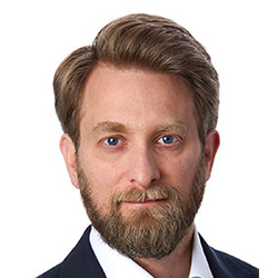 A close-up headshot of Evan Geller wearing a suit.