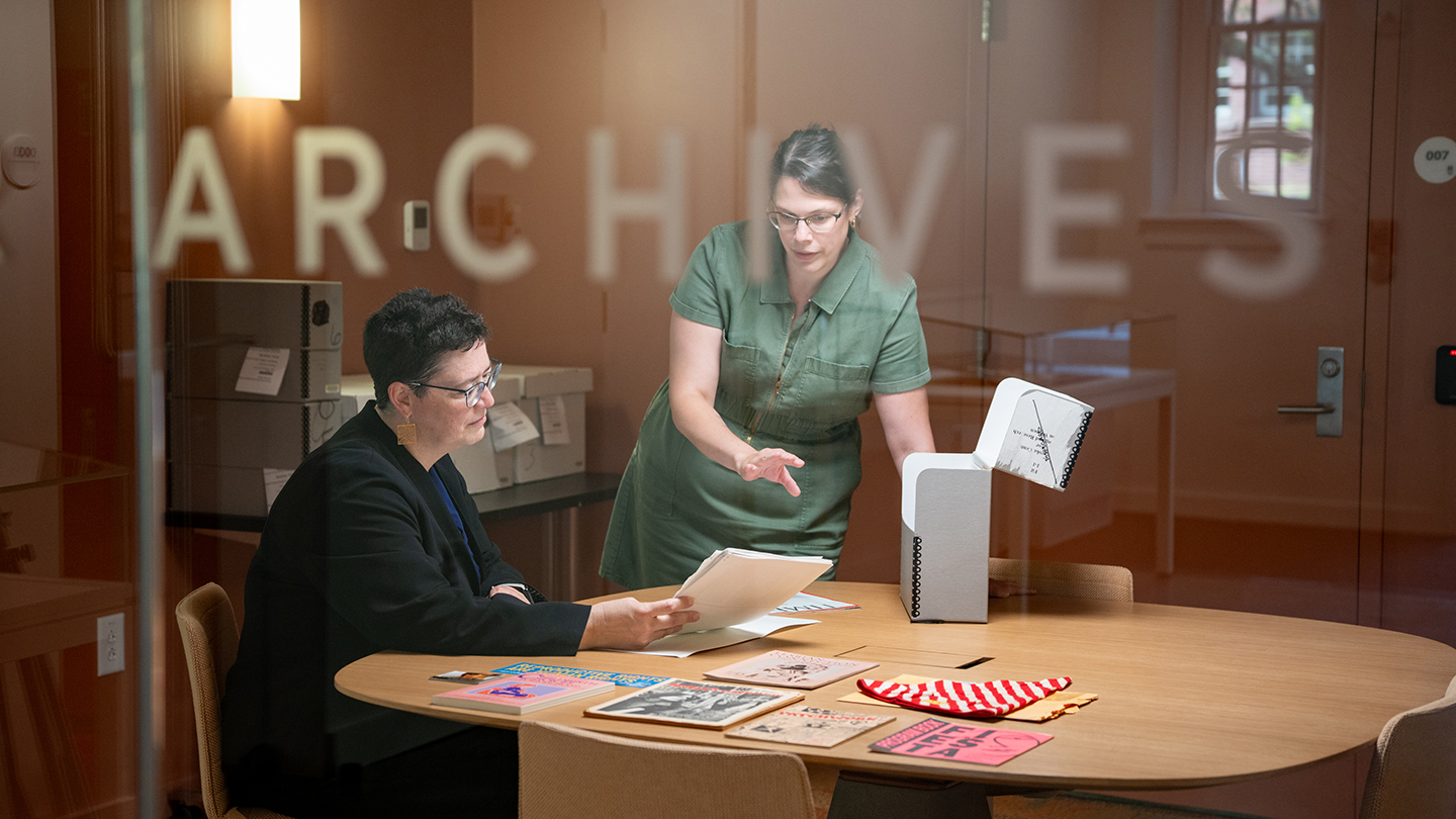 Leah VanWey is seated at a table in the archives, looking at a paper with a woman who stands beside her.