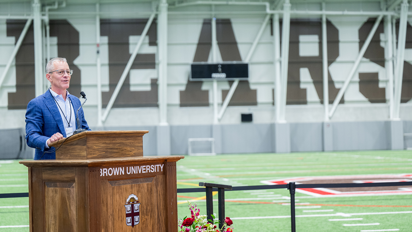 Greg Penner speaking at podium inside the Penner Field House during the dedication event.