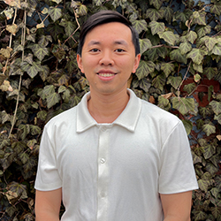 Yen Tran smiling, standing in front of a wall of ivy.
