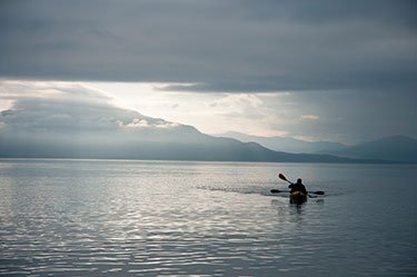 silhouette of person kayaking on a lake with mountain in background