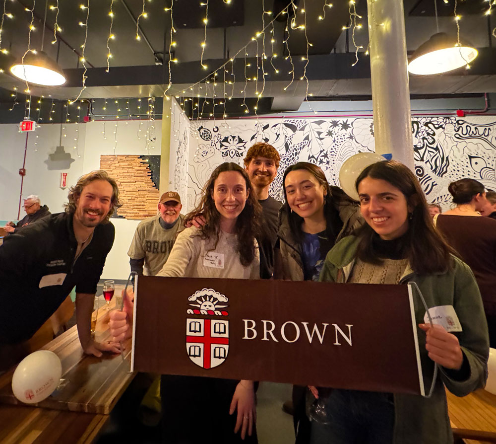 A group of students and alumni standing together holding a Brown University banner