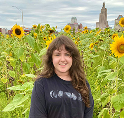 Photo of Olivia Watson standing in front of sunflowers.