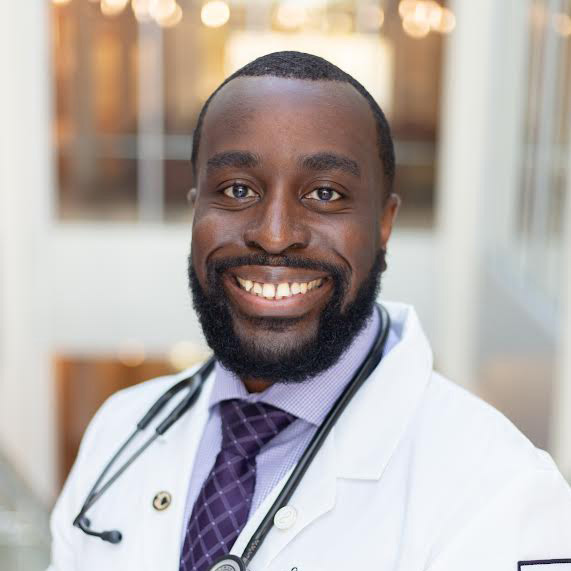 Elias Eteshola posing in white coat with stethoscope