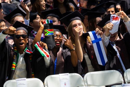 Four students at Brown Commencement raising flags and stoles representing their home countries.