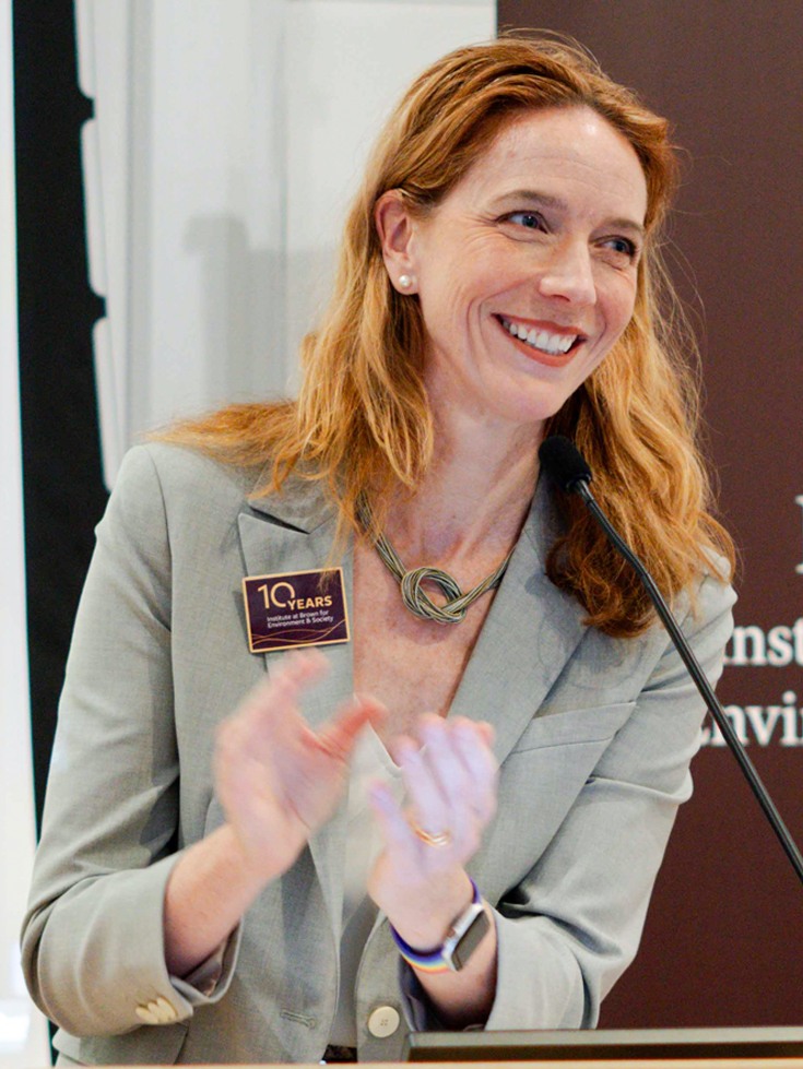Kim Cobb, director of the Institute at Brown for Environment and Society, clapping behind a podium.