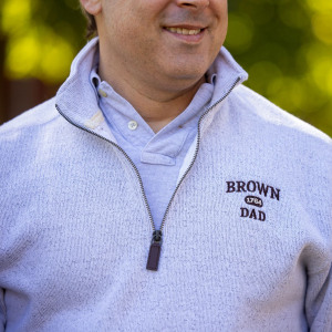 A man wearing a quarter zip sweater that reads Brown dad.