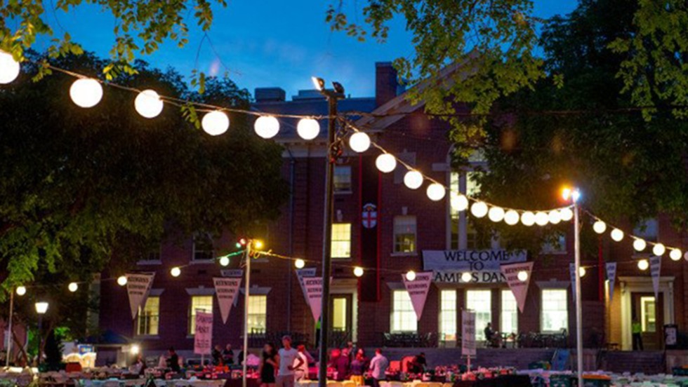 Campus dance at dusk with lit-up strings of lanterns hanging between trees