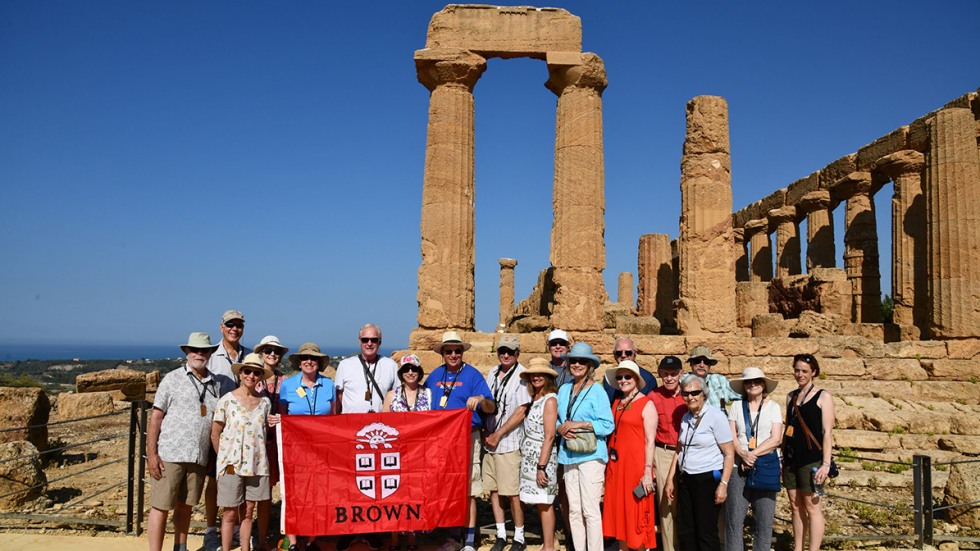 Alumni posing with Brown University banner in front of ancient ruin