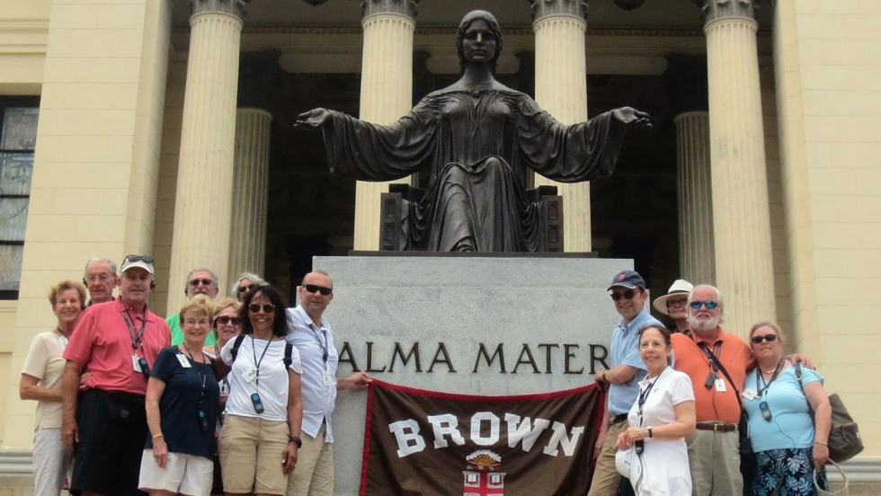 Alumni posing with Brown University banner in front of Alma Mater statue