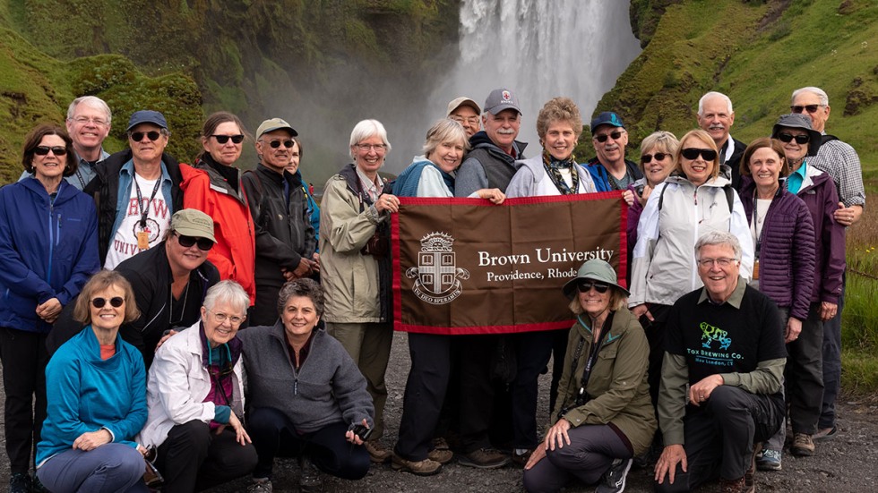 Alumni posing with Brown University banner in front of a waterfall in Iceland