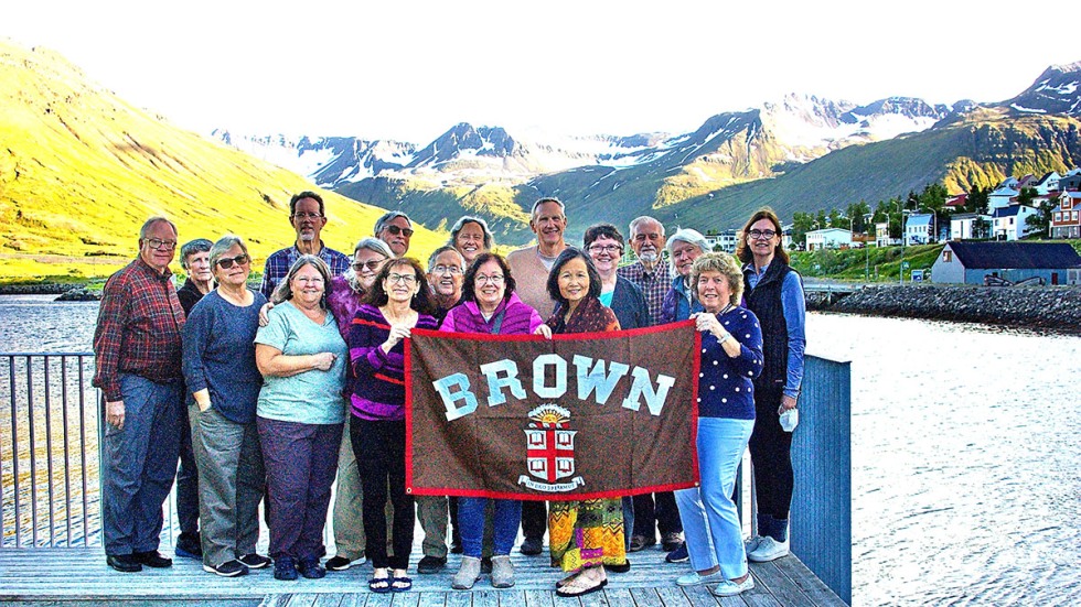 Alumni posing with Brown University banner on a lake in front of mountains in Iceland