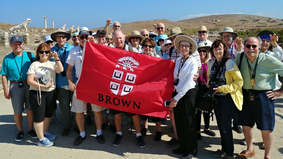 Alumni posing with Brown University banner in Greece at the Terrace of the Lions