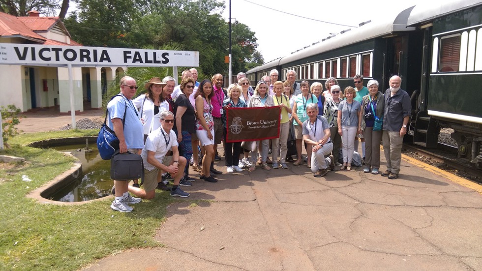 Alumni posing with Brown University banner at Victoria Falls train station
