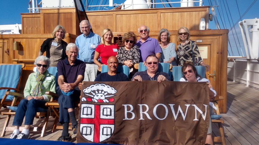 Alumni posing with Brown University banner on a yacht on Sicily