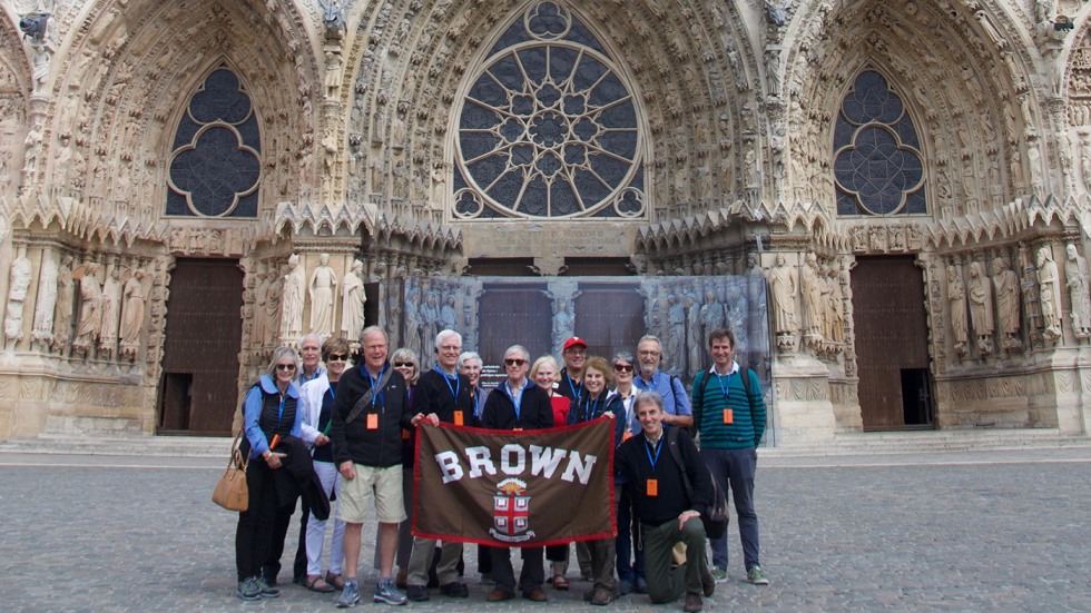 Alumni posing with Brown University banner in front of Notre Dame Cathedral