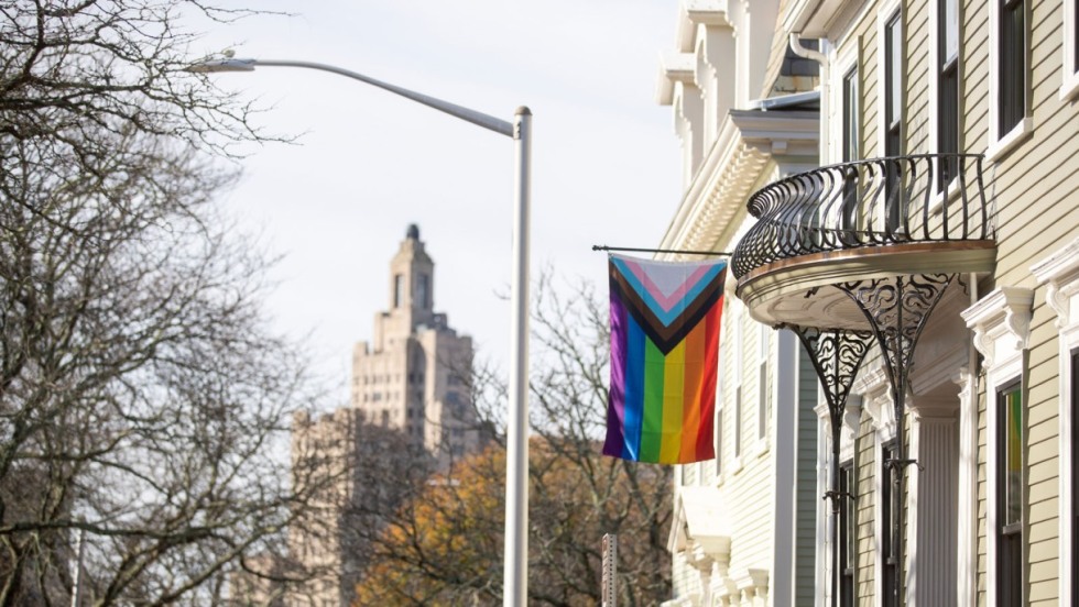 Stonewall House with Progress Pride flag hanging in front and downtown Providence building in the background