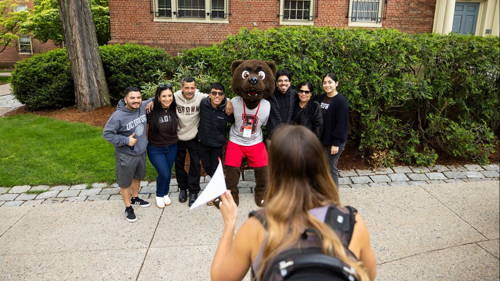 Bruno posing for a photo with seven Reunion attendees while a person in the foreground takes a picture.