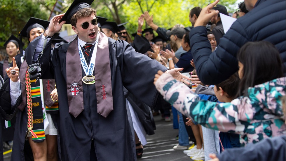 A member of the Class of 2025 wearing a cap and gown getting high fives from those lined up during Procession.