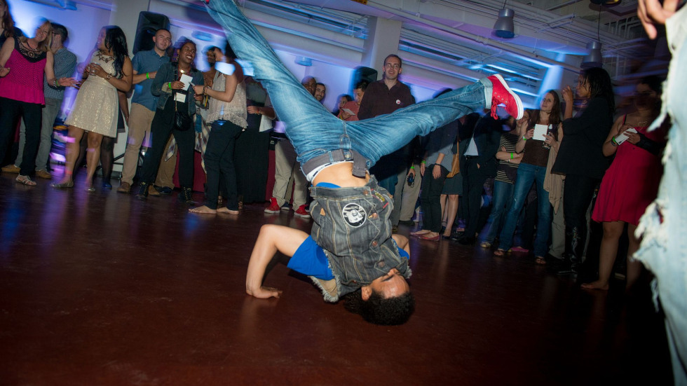 A person breakdancing energetically on the floor in a lively, crowded room with other partygoers. 