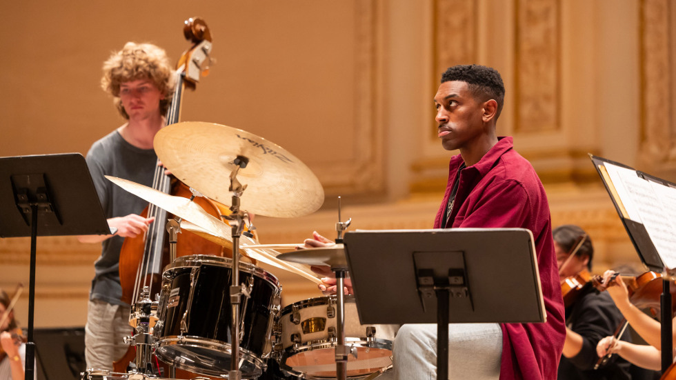 One musician plays a drum set while the other plays an upright bass during rehearsals. 