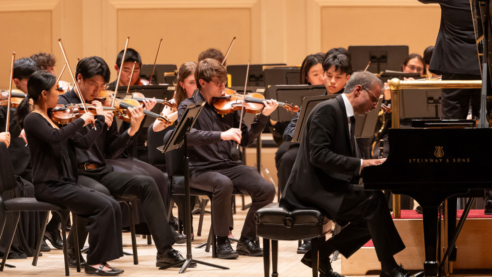 Saleem plays on stage while the orchestra sits behind, performing with string instruments. 