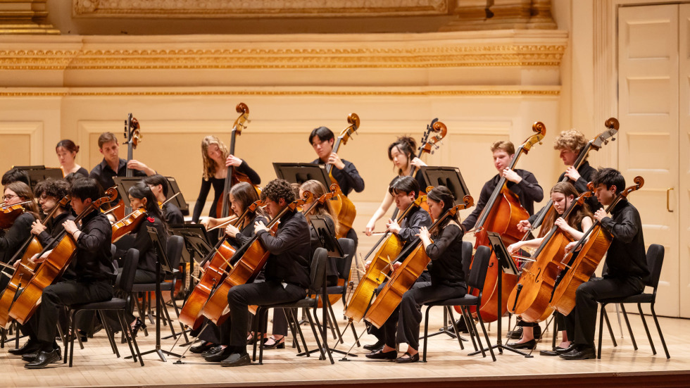 Brown Orchestra members seated in rows, playing string instruments. 