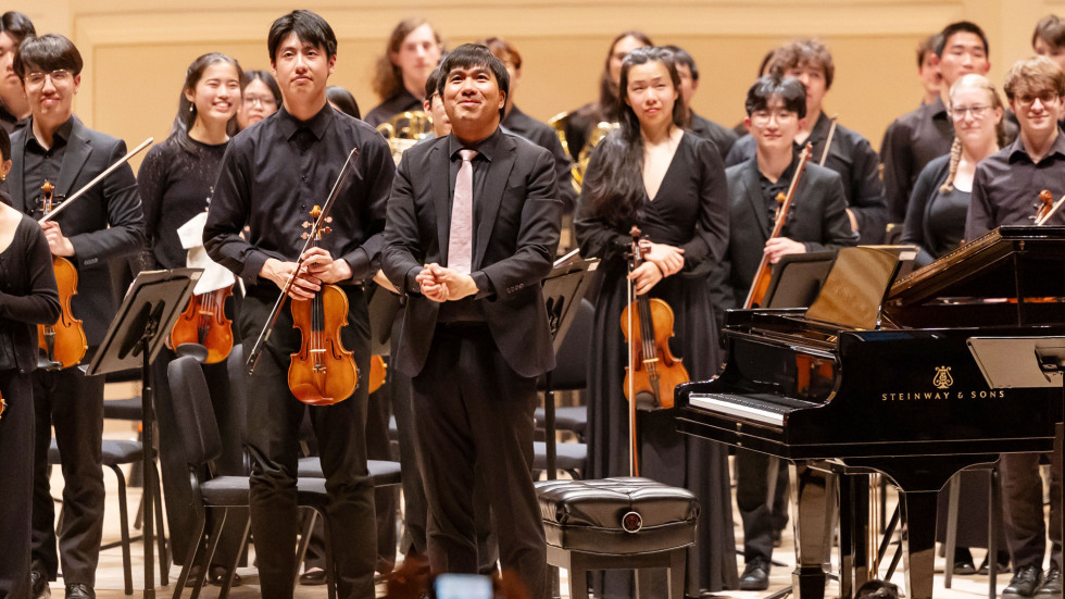 Orchestra and conductor standing together on stage at the end of their performance at Carnegie Hall. 