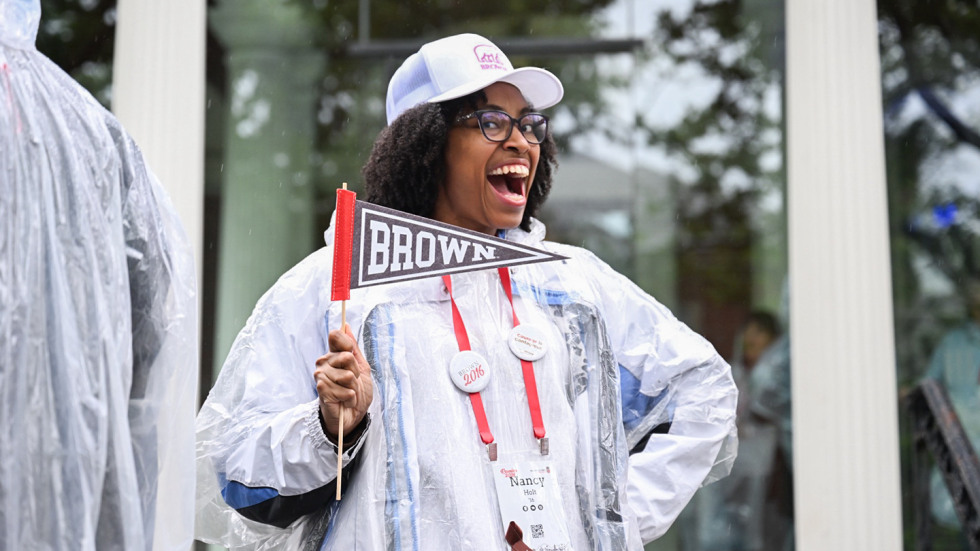 A woman wearing a poncho is smiling and holding a Brown pennant