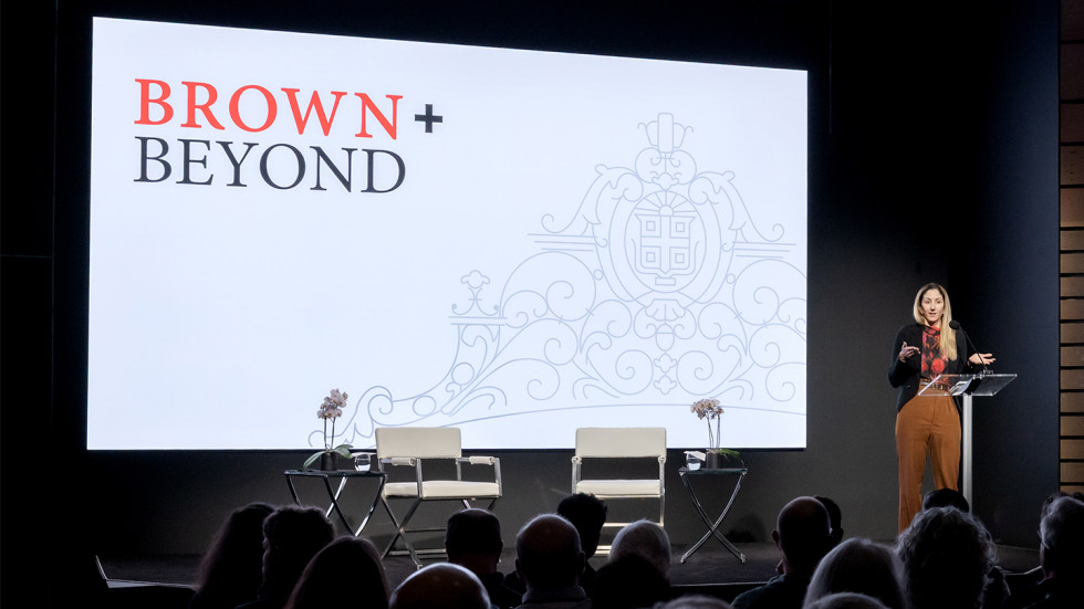 Aliisa Rosenthal ’05 speaking at the podium, with a Brown+Beyond-branded slide behind her.