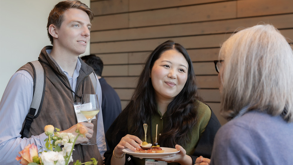 Three attendees at the event chatting while holding food and drinks.