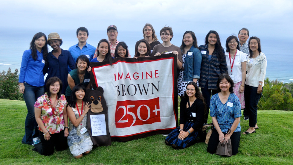 A group shot of Brown alums in Hawaii surrounding a banner that reads "Imagine - Brown 250+"